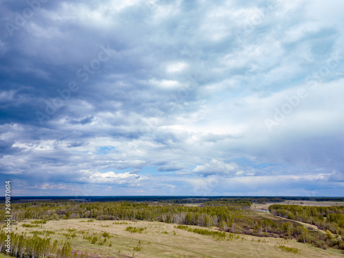 Aerial view of a landscape with green fields and forest under gray clouds and clouds on a warm spring day. Nature and the environment without people and harmful emissions.