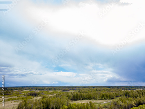 Aerial view of a landscape with green fields and forest under gray clouds and clouds on a warm spring day. Nature and the environment without people and harmful emissions.