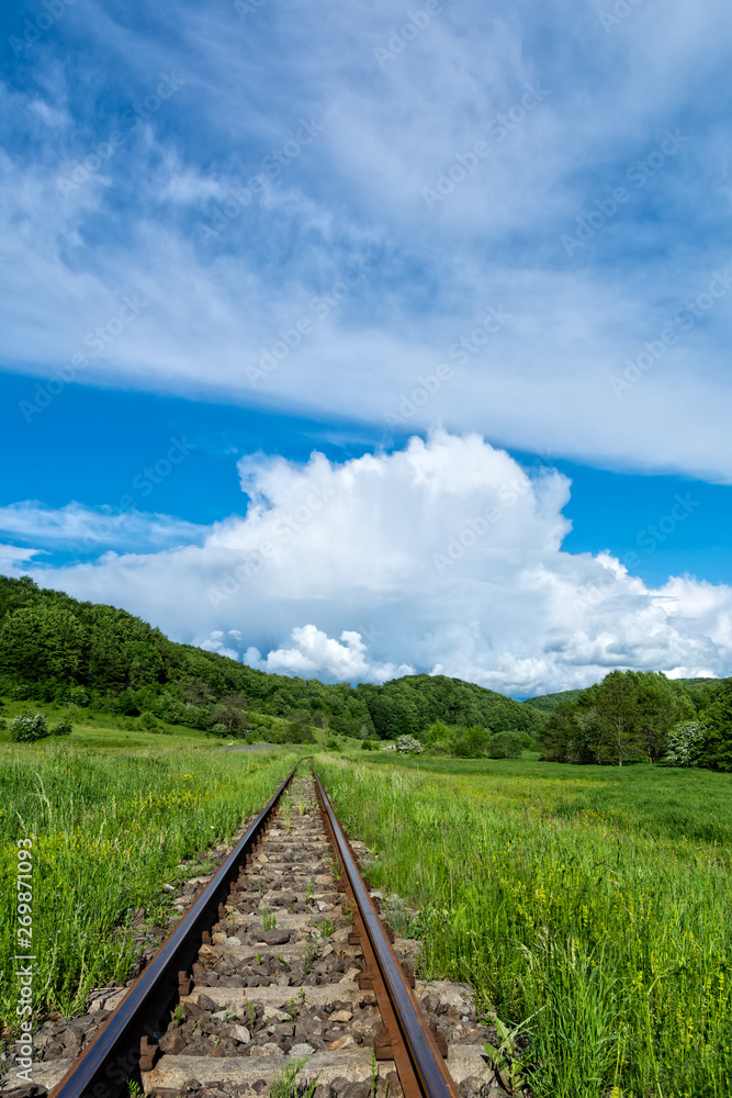 Railroad tracks with beautiful blue sky and green hills and forest