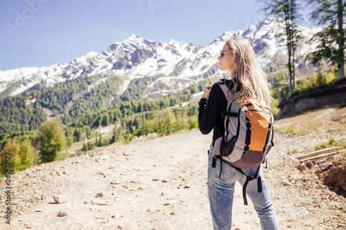Rear view of a beautiful young independent girl blonde traveler travels with a backpack in the mountains. Concept of desire for solitude and freedom.
