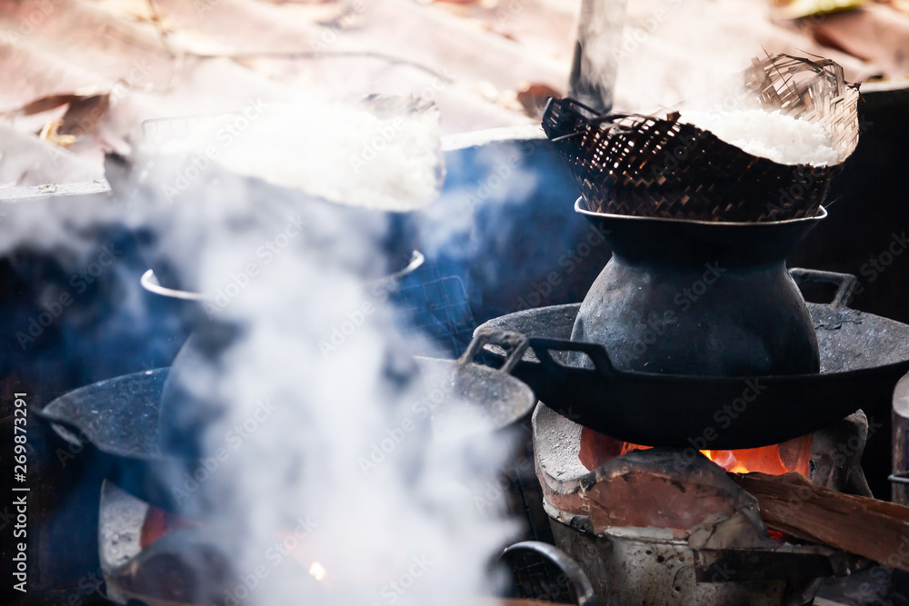 Cooking sticky rice on the traditional bamboo cone steamer on firewood