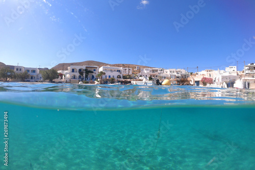 Underwater sea level photo of idilic pebble beach of Karavostasis, picturesque port of Folegandros island with traditional fishing boats docked and crystal clear turquoise sea, Cyclades, Greece © aerial-drone