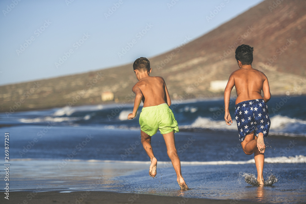 Back view of two young boys running on the beach after the end of school. Students enjoying summer vacation evening playing on the seashore. Schoolmates runs happy. Concept of freedom and happiness