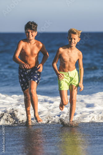 Portrait of two young boys playing at the beach after the end of school Couple of friends running together on the seashore Schoolmates enjoying holiday and summer vacation Concept of freedom happiness
