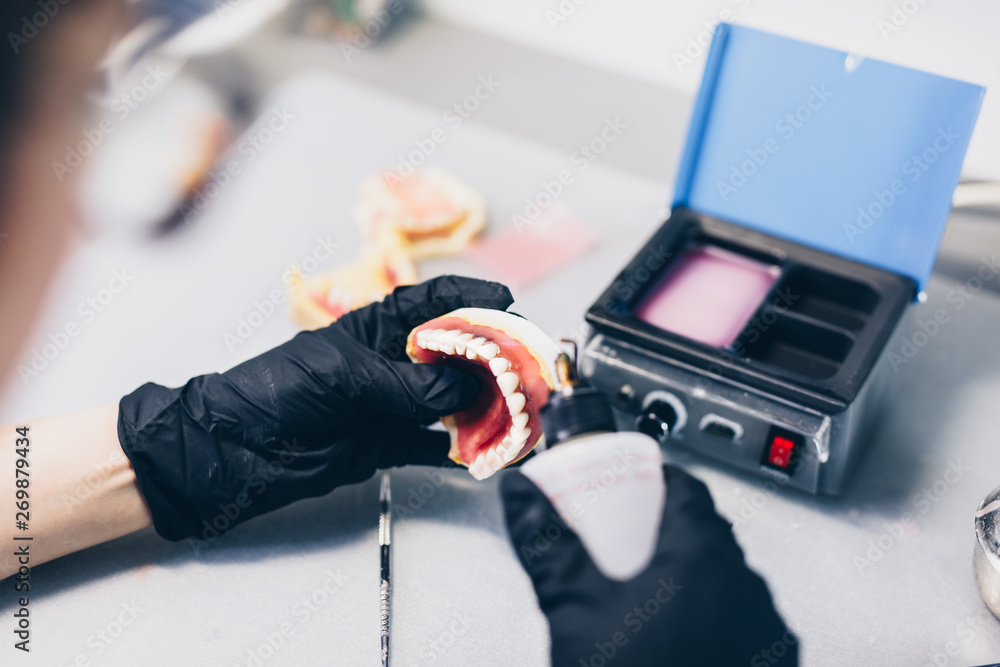 Fototapeta premium Dental prosthesis, prosthetics work. Close up of prosthetist hands while working on the denture. Selective focus.