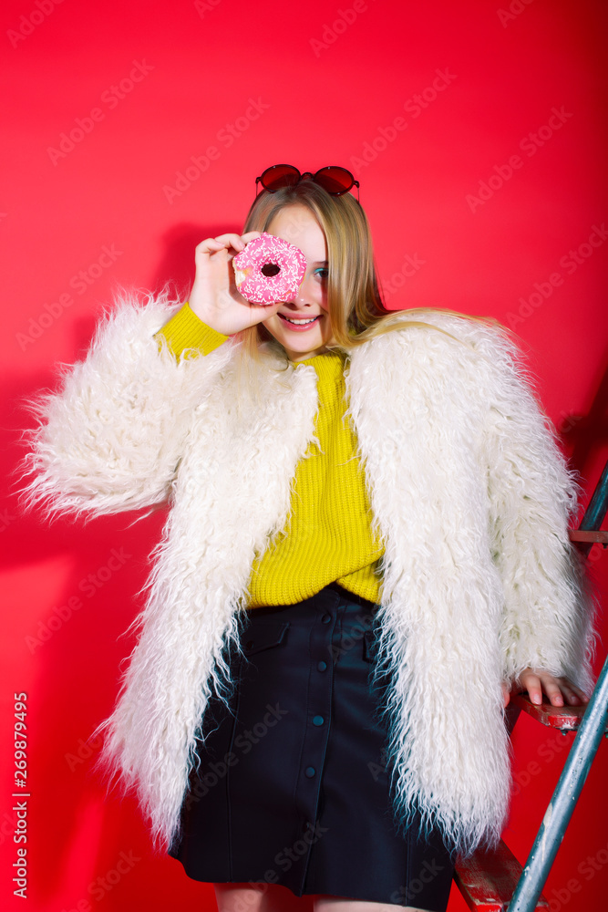little cute blond teenage girl posing in fashion style with donut on red background, lifestyle people concept little cute blond teenage girl posing in fashion style with donut on red background, lifestyle people concept