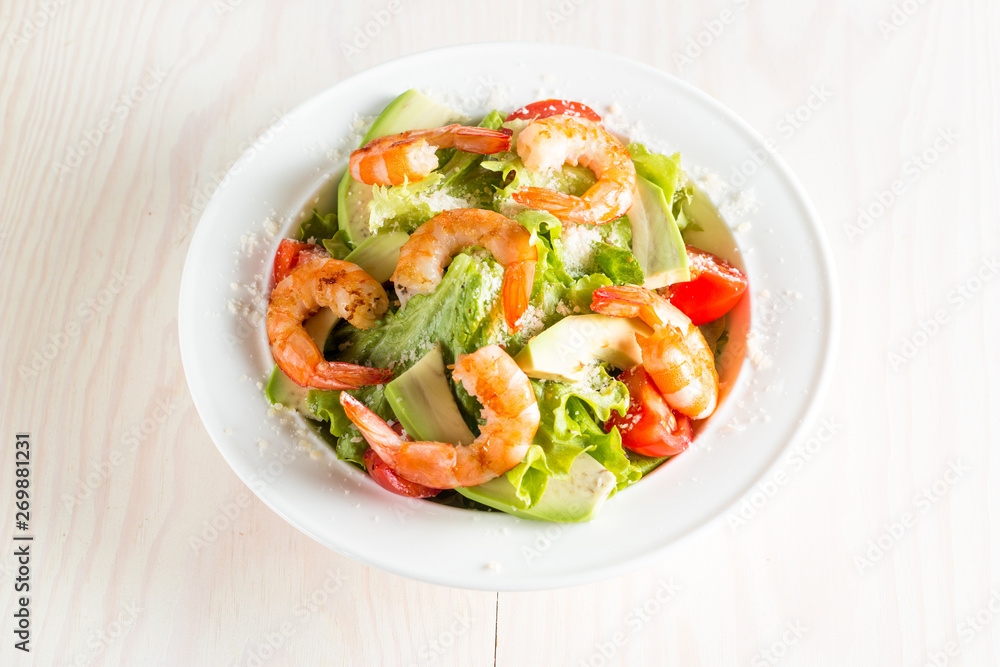 Fresh shrimp salad made of tomato, ruccola, avocado, prawns, chicken breast, arugula, crackers and spices. Caesar salad in a white, transparent bowl on wooden background Fresh shrimp salad made of tomato, ruccola, avocado, prawns, chicken breast, arugula, crackers and spices. Caesar salad in a white, transparent bowl on wooden background