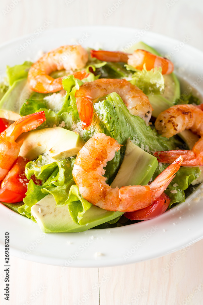 Fresh shrimp salad made of tomato, ruccola, avocado, prawns, chicken breast, arugula, crackers and spices. Caesar salad in a white, transparent bowl on wooden background Fresh shrimp salad made of tomato, ruccola, avocado, prawns, chicken breast, arugula, crackers and spices. Caesar salad in a white, transparent bowl on wooden background