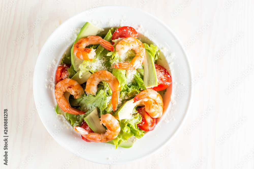 Fresh shrimp salad made of tomato, ruccola, avocado, prawns, chicken breast, arugula, crackers and spices. Caesar salad in a white, transparent bowl on wooden background Fresh shrimp salad made of tomato, ruccola, avocado, prawns, chicken breast, arugula, crackers and spices. Caesar salad in a white, transparent bowl on wooden background