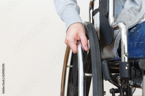 Detail of disabled woman holding a hand on wheel of a wheelchair.