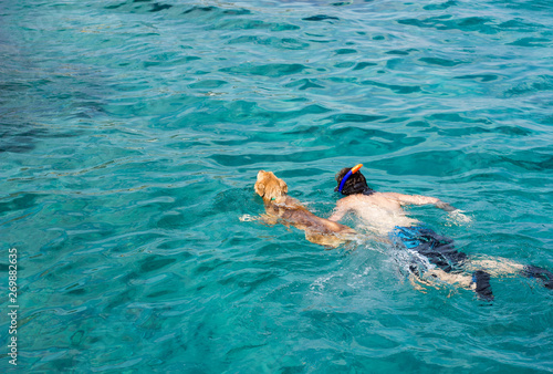 dog and boy swimming and vivid blue water of Red sea scenic natural environment, background pattern concept picture of friendship between human and animal, copy space 
