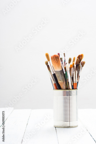 bunch of paint brush at tin can, on white wooden
