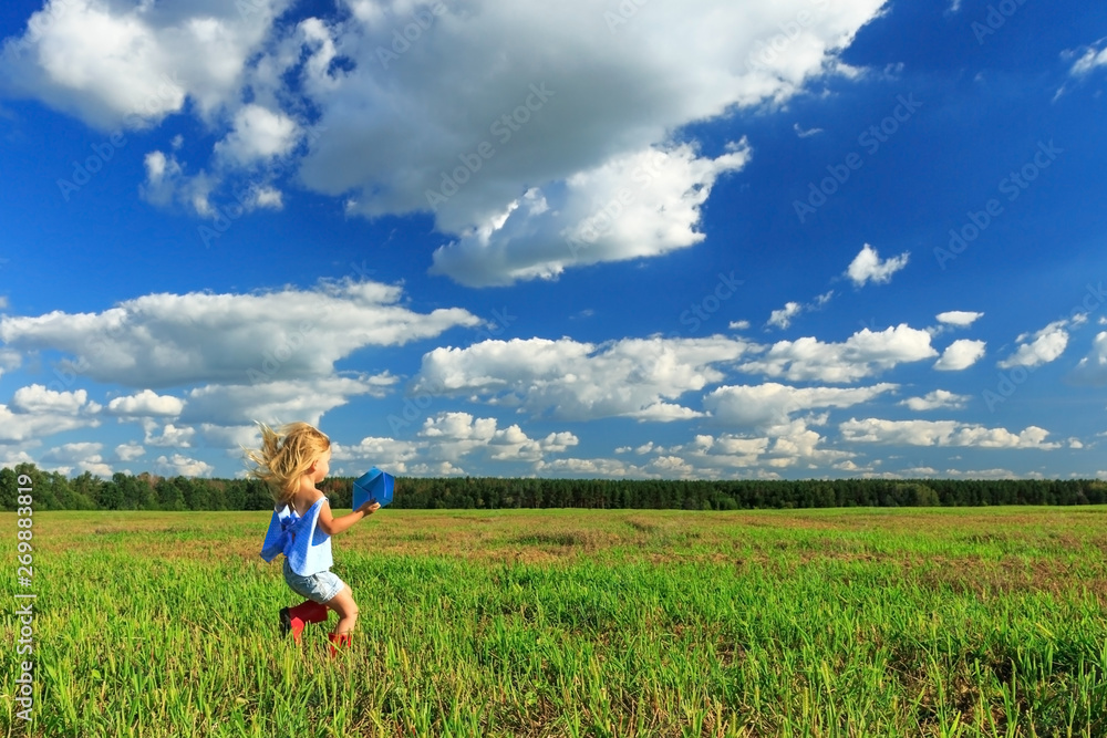 Little girl holding a paper plane in a hand and running in a field.