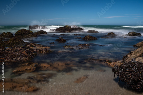 Waves crashing over rocks on the jagged coastline of Northern California, taken on a long exposure to smooth out the water and create beautiful smooth effect, against a bright blue sky