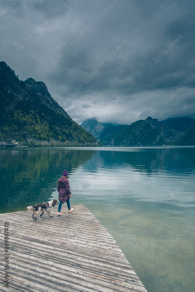 Kobieta z psem Springer Spanielem stoją na pomoście nad górskim jeziorem w pochmurny dzień	