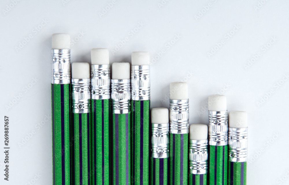 many simple pencils with erasers with green skin in a row on a white table many simple pencils with erasers with green skin in a row on a white table