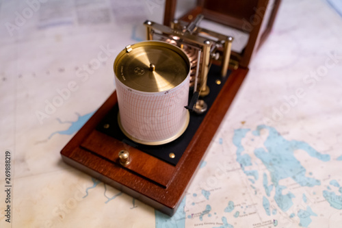 Vintage marine barograph with opened cover standing on a navigational chart
