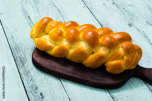fresh challah bread on cutting board, blue wooden table