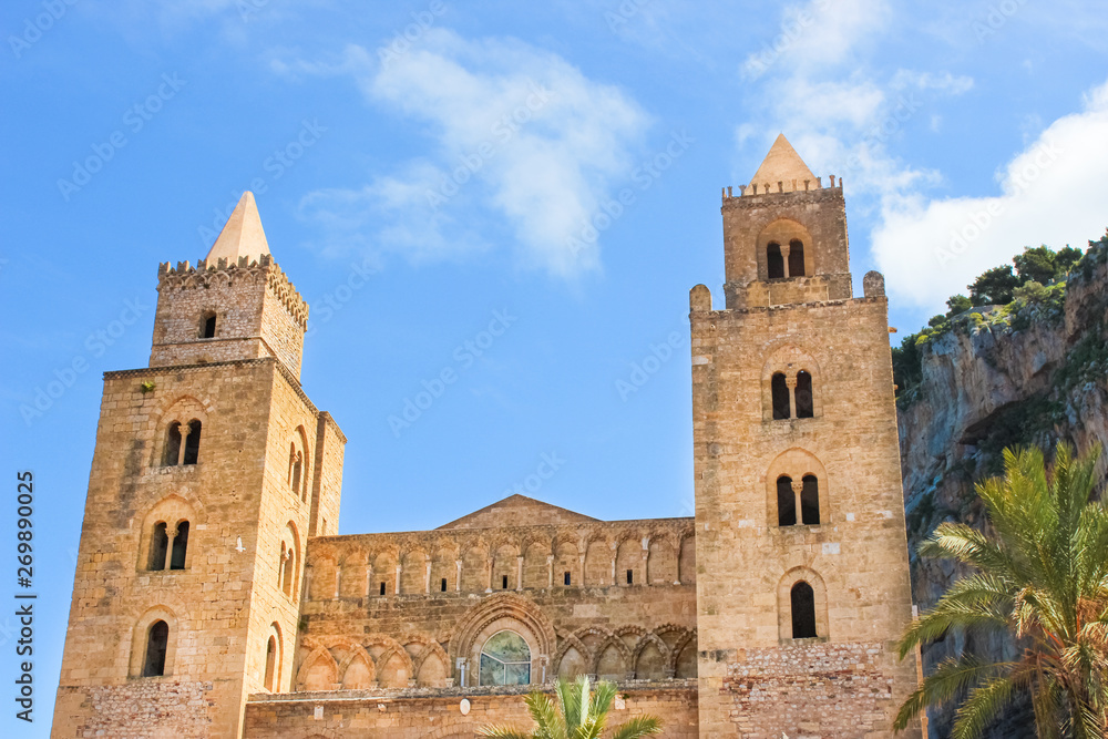 Cefalu Cathedral in Sicily, Italy with blue sky and rocks behind. Famous Roman Catholic basilica erected in Norman architectural style. Part of UNESCO World Heritage and popular attraction