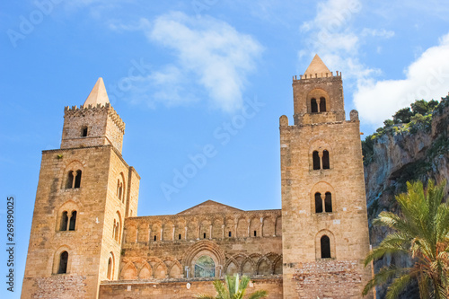 Cefalu Cathedral in Sicily, Italy with blue sky and rocks behind. Famous Roman Catholic basilica erected in Norman architectural style. Part of UNESCO World Heritage and popular attraction