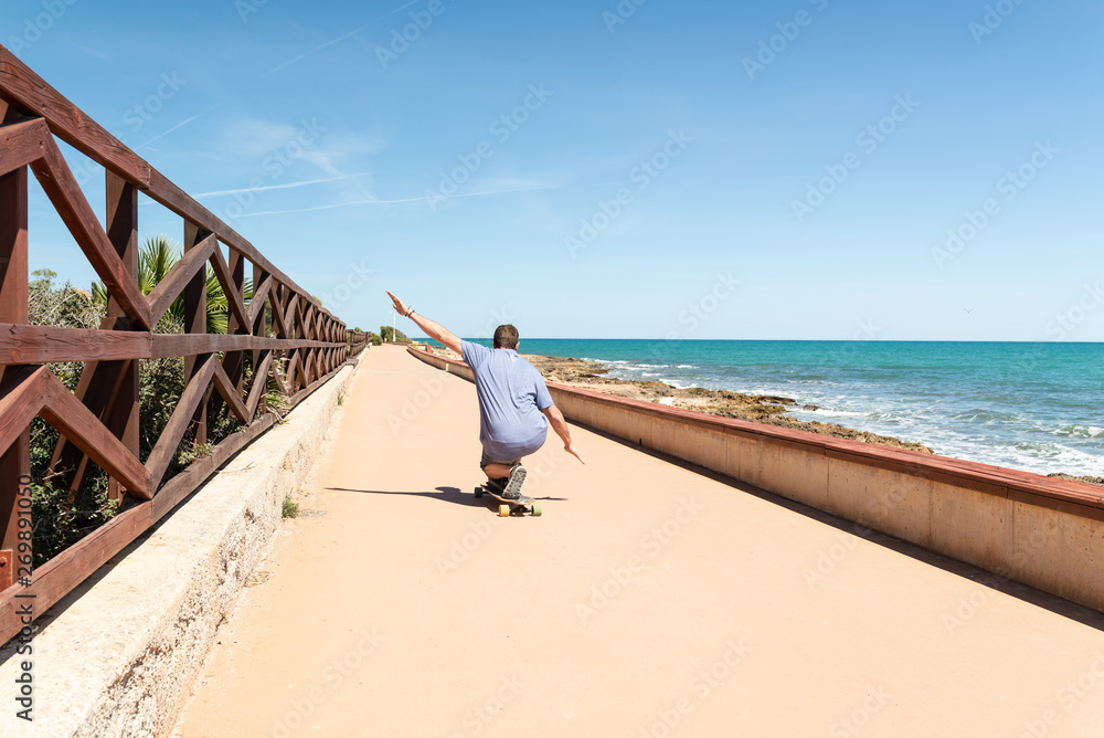 Man having fun with a longboard in a promenade close to the sea