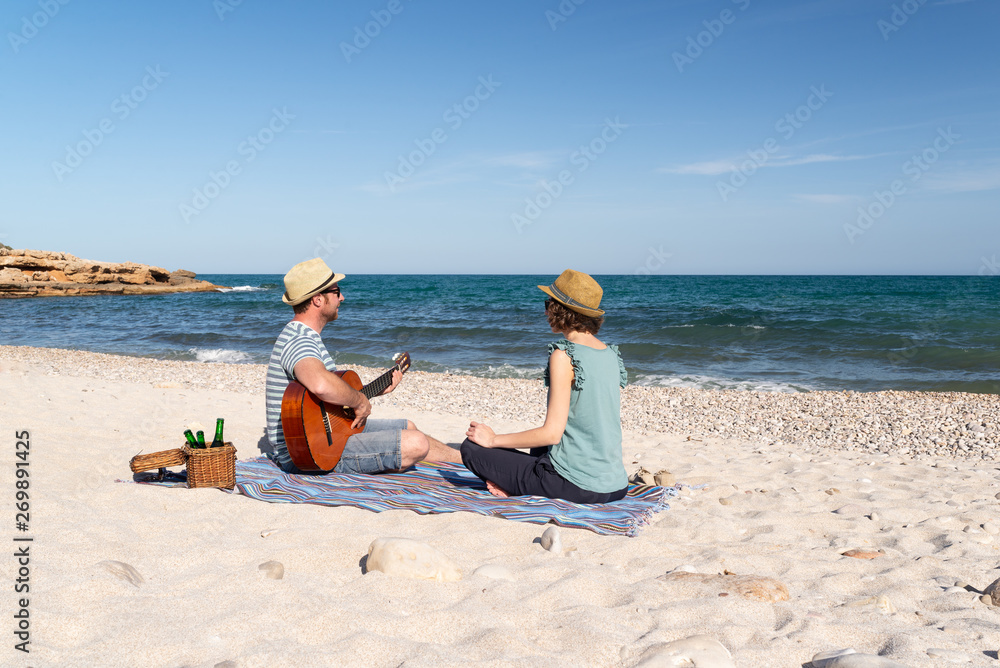 Couple of friends playing the guitar and having fun on a beach at sunset. Mediterranen coast