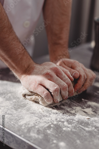 Professional baker kneads dough on the table in the kitchen of the bakery © Leika production