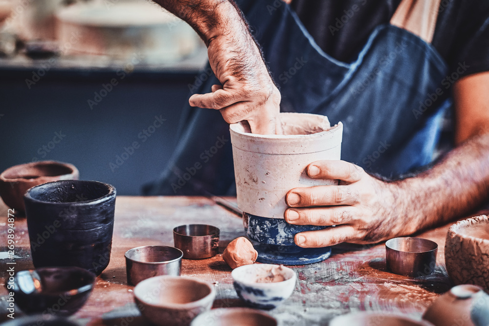 Man is putting colourful clay to his new handmade pot.
