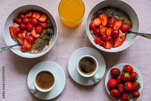 Vegan breakfast for two with a bowl of oatmeal porridge with fresh strawberries, chia and ground flax seeds, coffee and freshly squeezed orange juice. Plant based diet concept. Top view.