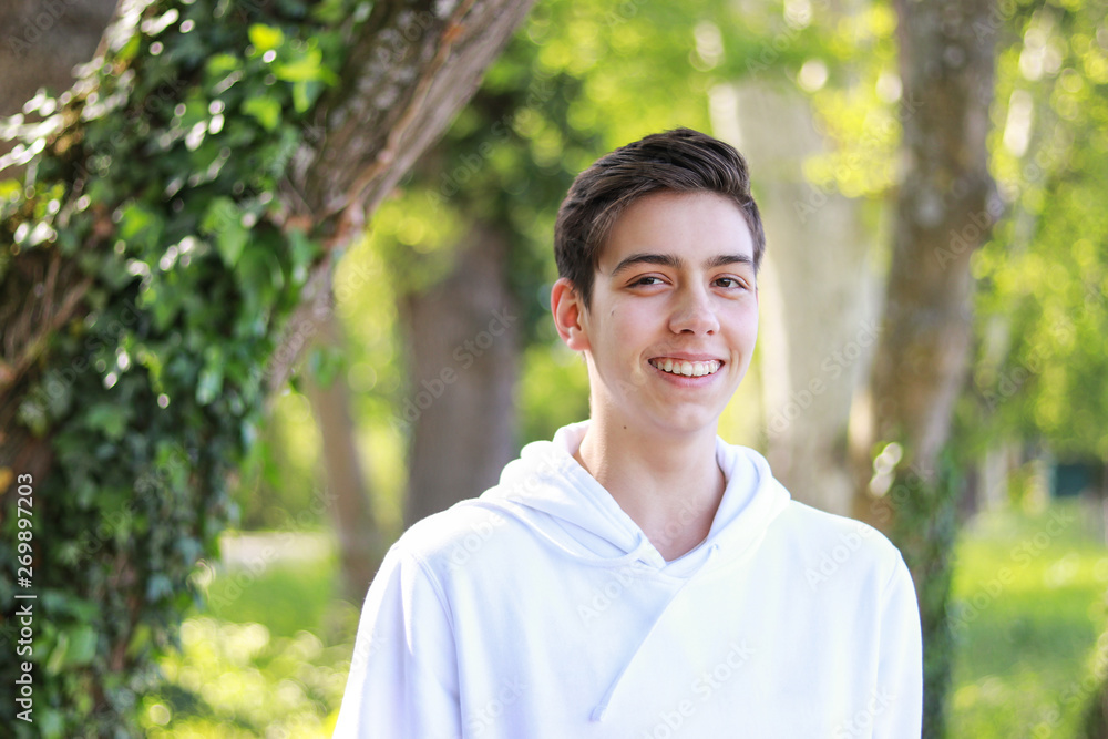 Close-up portrait of happy smiling handsome teenager boy in white hoody in park outdoors at bright sunny day. Close-up portrait of happy smiling handsome teenager boy in white hoody in park outdoors at bright sunny day.