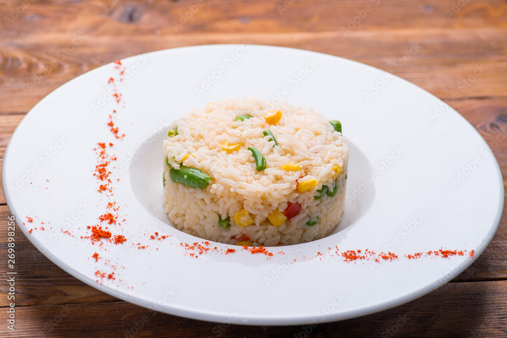 boiled rice with vegetables in a white plate on a wooden table boiled rice with vegetables in a white plate on a wooden table