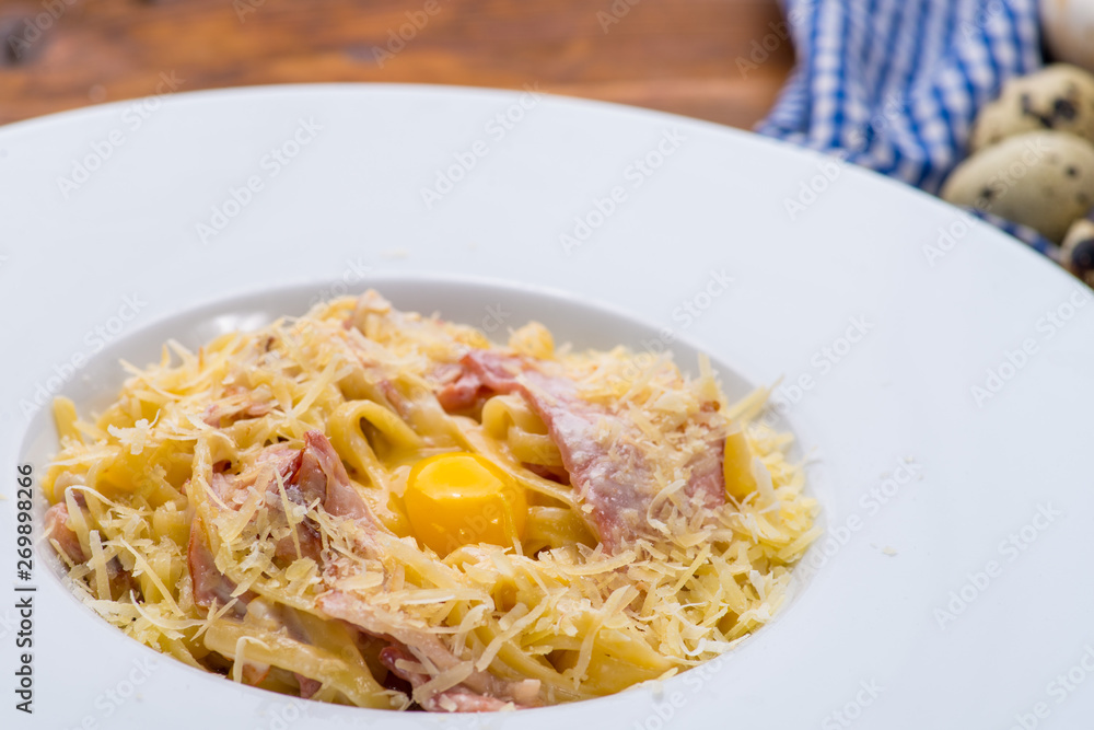 Carbonara pasta with egg yolk in a white plate on a wooden background