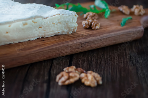 Brie cheese, walnuts and arugula on a brown wooden board.