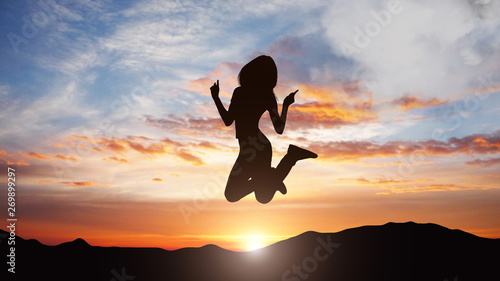 Silhouette of jumping woman against sunset background