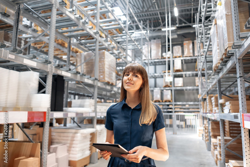 Wholesale warehouse. Beautiful young woman worker of store in shopping center. Girl looking for goods with a tablet is checking inventory levels in a warehouse. Logistics concept