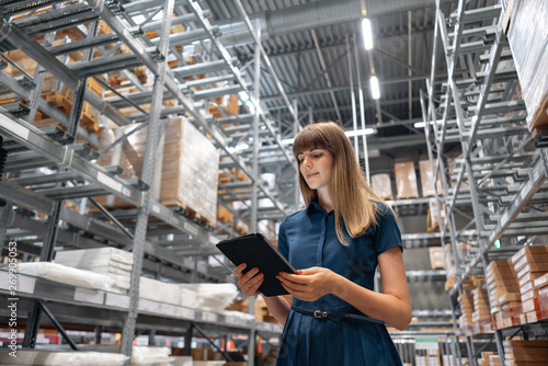 Wholesale warehouse. Beautiful young woman worker of store in shopping center. Girl looking for goods with a tablet is checking inventory levels in a warehouse. Logistics concept