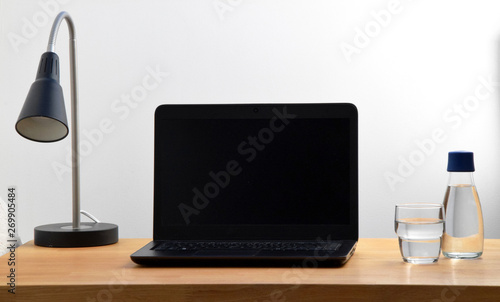 Home office with lamp  laptop  water bottle and glass of water on wooden table