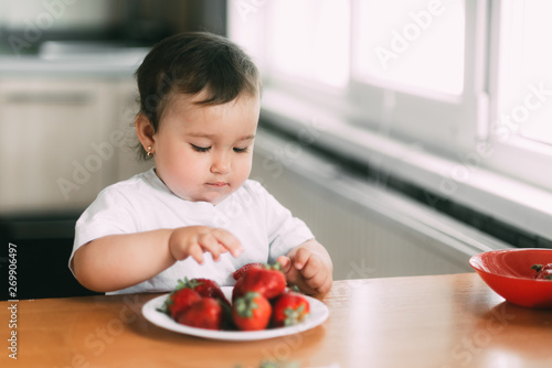 Little girl child in white t-shirt eating strawberries all smeared and dirty