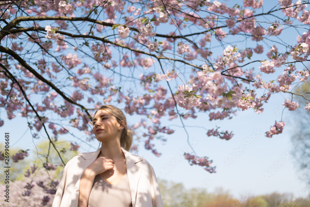 Beautiful blonde young woman in Sakura Cherry Blossom park in Spring enjoying nature and free time during her traveling tourist free time - Wearing white pants and t-shirt with a beige jacket Beautiful blonde young woman in Sakura Cherry Blossom park in Spring enjoying nature and free time during her traveling tourist free time - Wearing white pants and t-shirt with a beige jacket
