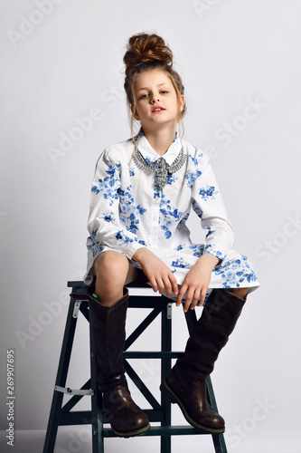Pretty fashionable kid girl teenager in modern dress and high boots is  sitting on black stepladder Stock Photo | Adobe Stock