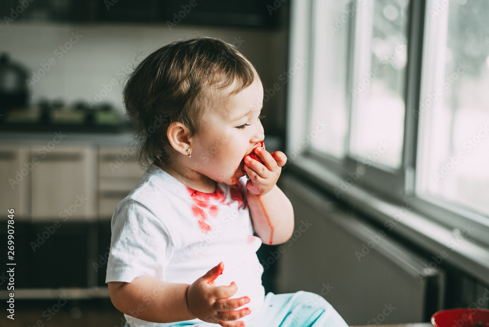 A little girl in a white t-shirt all dirty climbed on the table sitting and eating strawberries A little girl in a white t-shirt all dirty climbed on the table sitting and eating strawberries
