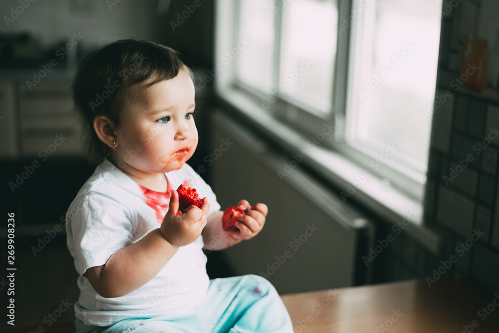 A little girl in a white t-shirt all dirty climbed on the table sitting and eating strawberries A little girl in a white t-shirt all dirty climbed on the table sitting and eating strawberries