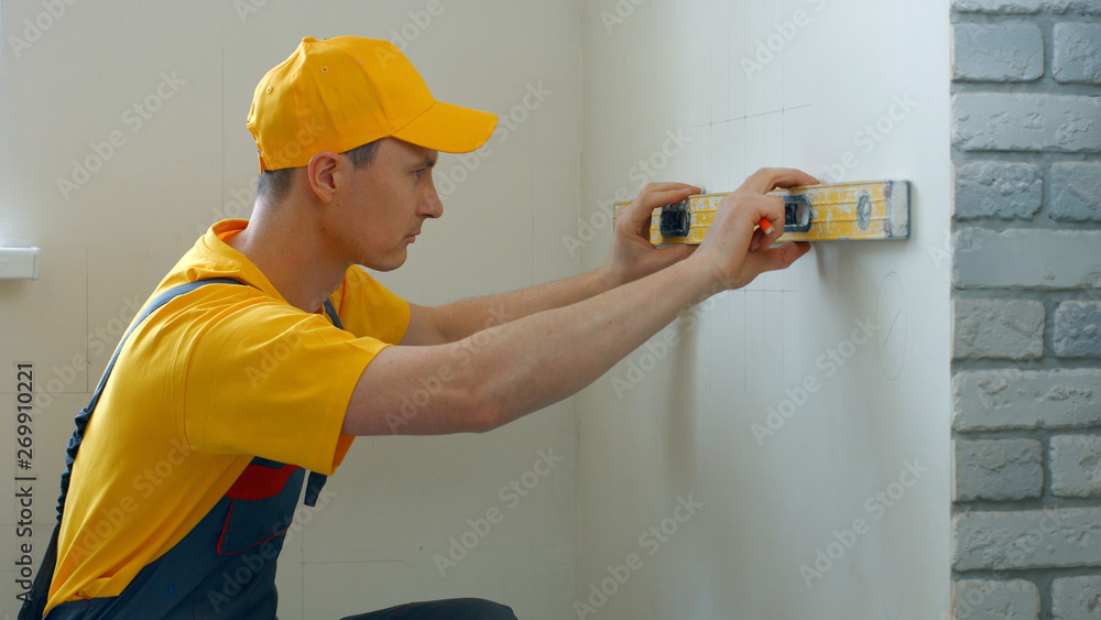 Caucasian builder measuring wall with level tool. Young repairman measuring wall with builder level. House renovation concept. Caucasian builder measuring wall with level tool. Young repairman measuring wall with builder level. House renovation concept.