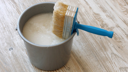 Wallpaper paste brush and grey bucket. Bucket with wallpaper glue and brush on new wooden floor. Apartment renovation concept.