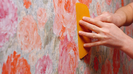 Contractor repairing apartment. Close up hand of decorator smoothing wallpaper using spatula. Home renewal concept.
