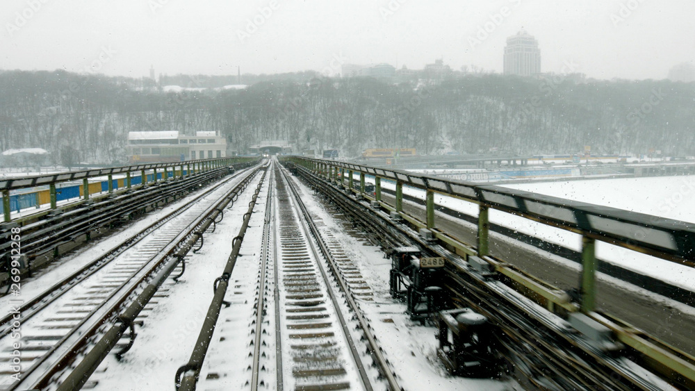 Train moves through the bridge at snow stormy day time. Train moves on bridge in winter season. Route of tube train.