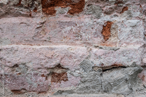 abstract background of an old brick wall with peeling plaster and the remains of pink paint close up