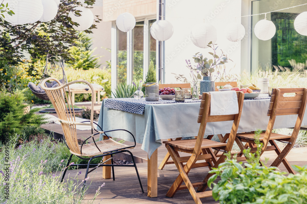 Table with wooden chairs in bright green garden of modern house, real photo - obrazy, fototapety, plakaty 