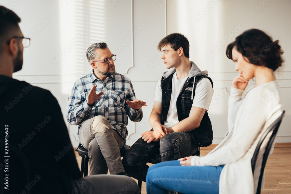 Psychologist talking about twelve-step program to addicted man during group support meeting Psychologist talking about twelve-step program to addicted man during group support meeting