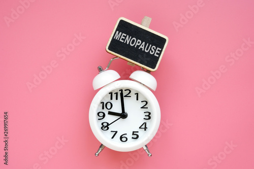 Alarm clock and word menopause on a pink background. photo